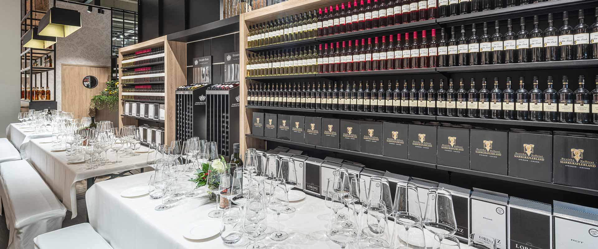 Nakryty stół na dziale z winami w Edeka Süllau w niemieckim Trittau oświetlony za pomocą projektora Kalo.