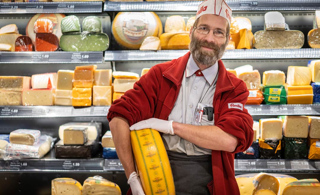 Specjalistyczny sprzedawca z gomółką sera na tle regału z serami. 